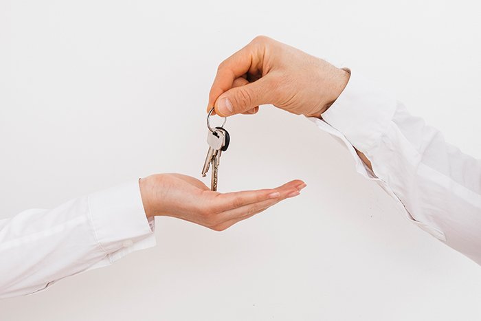 Hand agent with home in palm and key on finger. Offer of purchase house, rental of Real Estate. Giving, offering, demonstration, handing house keys.